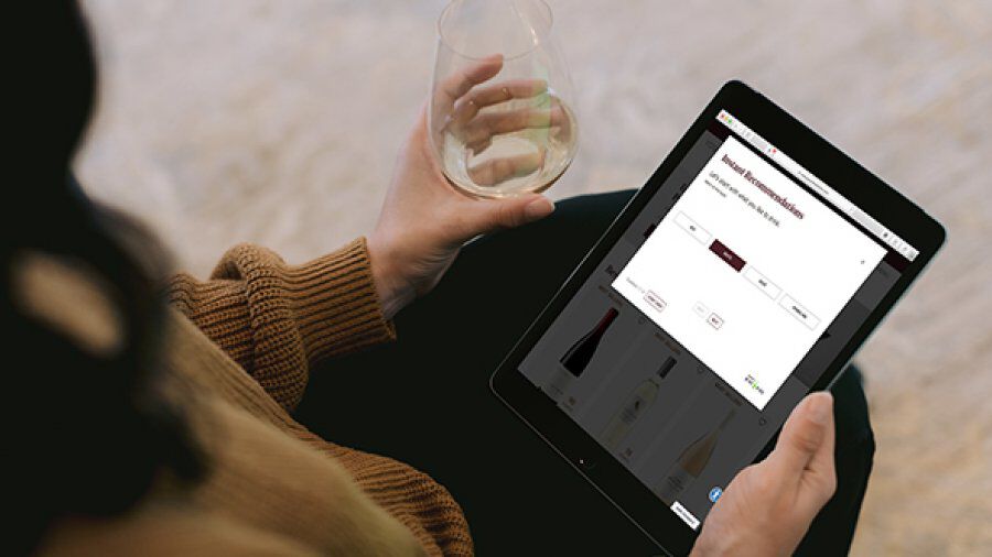 Person looking at tablet with glass of wine in hand.